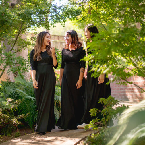 Three Choral and Sacred Music singers walk in a garden.