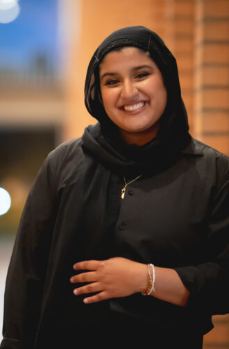 A USC Thornton choir member smiles for the camera, wearing a head scarf.