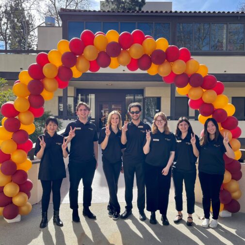 Student ambassadors gather under a balloon arch showing the hand sign for 'fight on.'