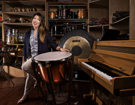A classical musician dressed in concert attire smiling and posing next to percussion equipment.