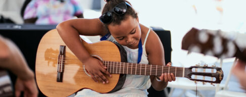 Photo of a young child learning how to play the guitar.