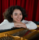 Thornton student Evangeliya Delizonas leans against a piano and smiles.