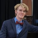 Pianist sits next to piano, facing the camera.