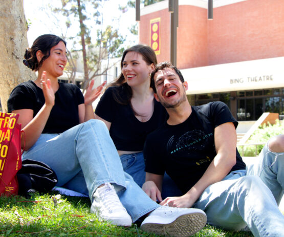 Three students sit on the lawn at the Thornton School of Music, laughing.