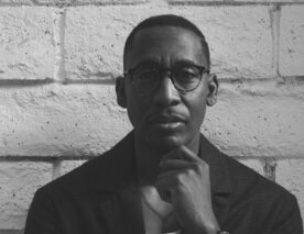 Black and white photo of producer Raphael Saadiq leaning against a wall