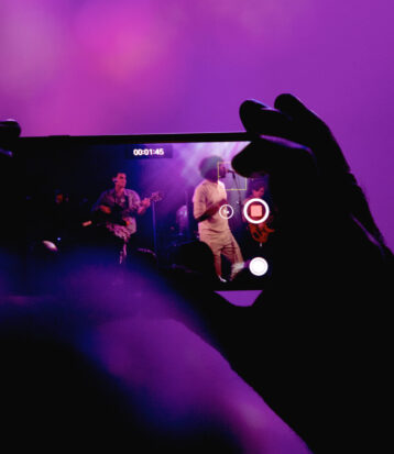 Image of blurred hands looking at popular music performers through an iPhone.