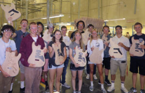 Students and instructors pose for a photo wearing safety glasses and holding unfinished guitars.