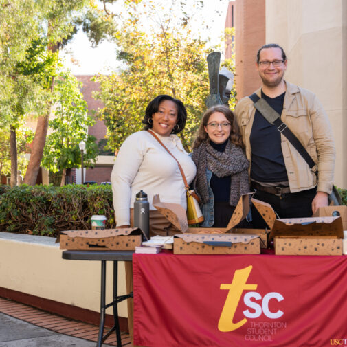 Three students smiling around an outdoor student council information booth.