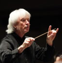 Conductor Carl St.Clair leads an ensemble with a baton in mid-air.