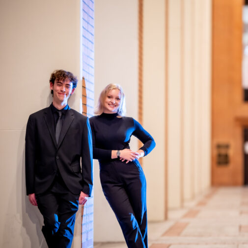 pair of choral students stand together outdoors.