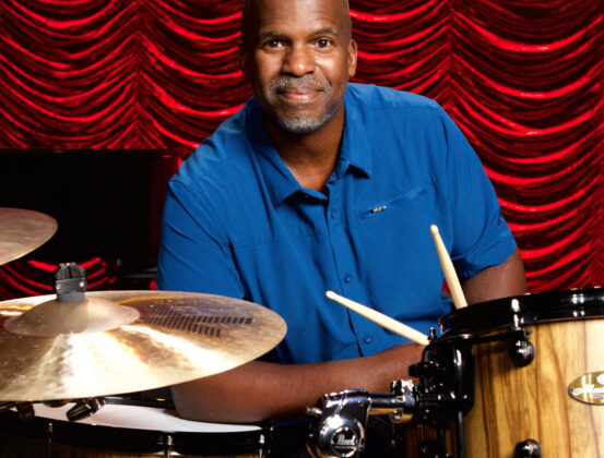 Will Kennedy seated at his drum kit, holding drum sticks.