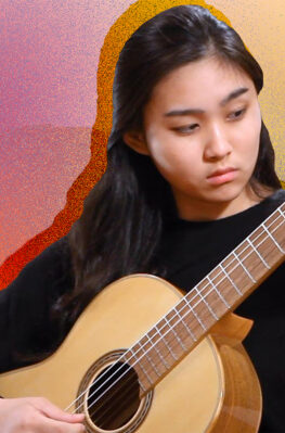 A classical guitarist plays her instrument in front of a brightly colored artistic background.