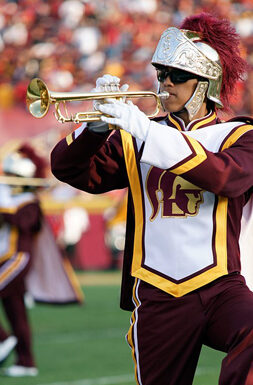 USC student plays trumpet on the football field in marching band attire.
