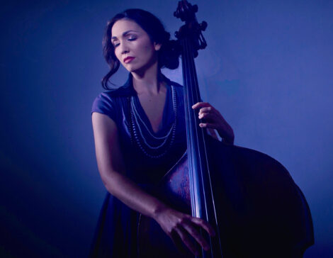 Katie Thiroux playing her double bass with a dark blue background.